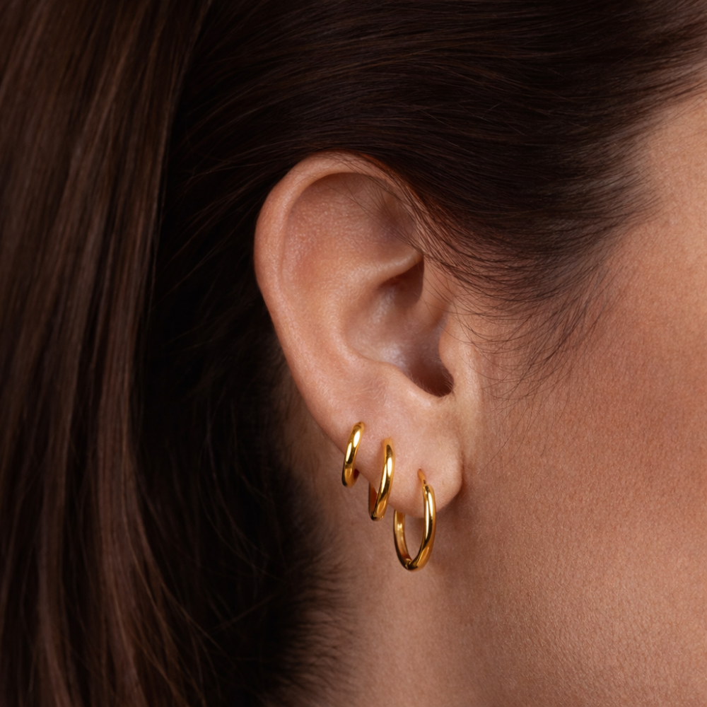 Kolczyki Sienna Huggies wykonane ze stali nierdzewnej pokrytej powłoką PVD w kolorze 14-karatowego złota – wodoodporne i odporne na matowienie kolczyki w kształcie kółek, dostępne w rozmiarach 15 mm, 18 mm i 20 mm.