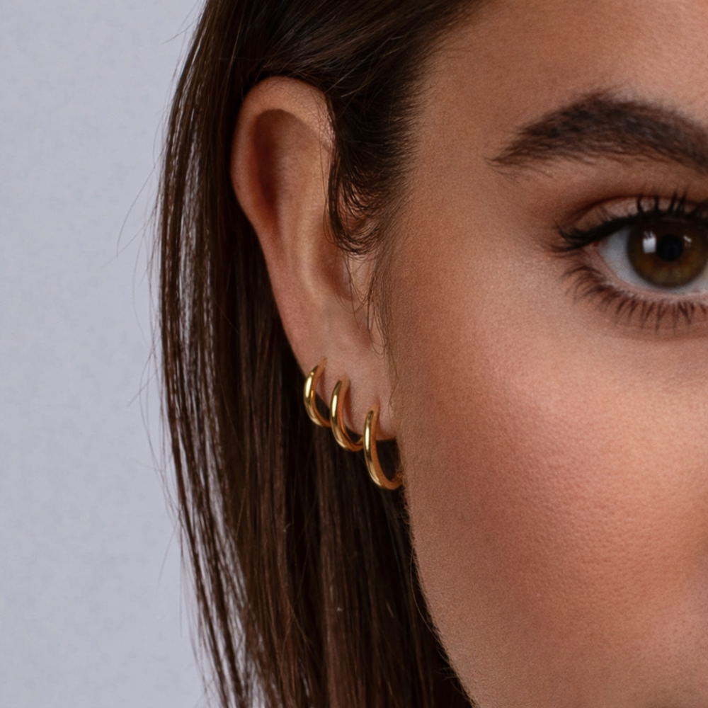 Kolczyki Sienna Huggies wykonane ze stali nierdzewnej pokrytej powłoką PVD w kolorze 14-karatowego złota – wodoodporne i odporne na matowienie kolczyki w kształcie kółek, dostępne w rozmiarach 15 mm, 18 mm i 20 mm.